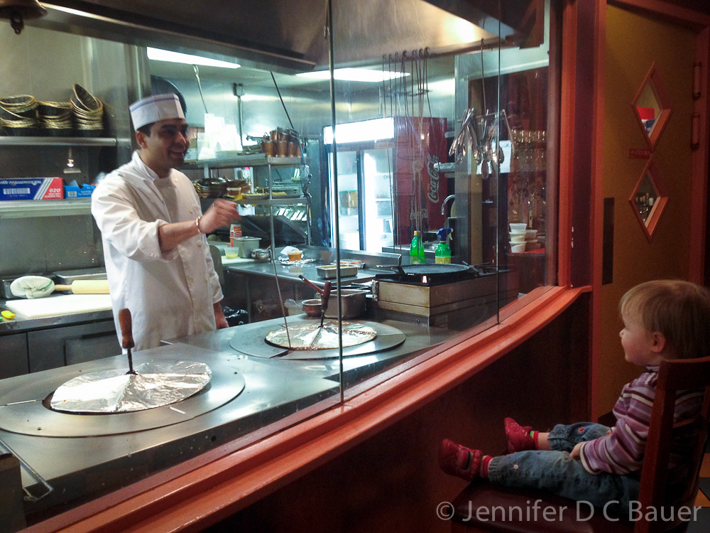 Addie watching the chef prepare food at Bollywood Grill.